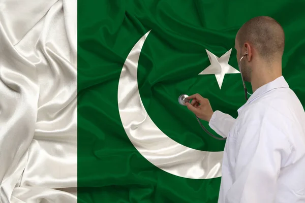 Photographie partielle d'un médecin en uniforme sur fond de drapeau national du Pakistan sur soie brillante délicate, concept de soins médicaux et d'assurance dans le pays, gros plan, espace de copie — Photo