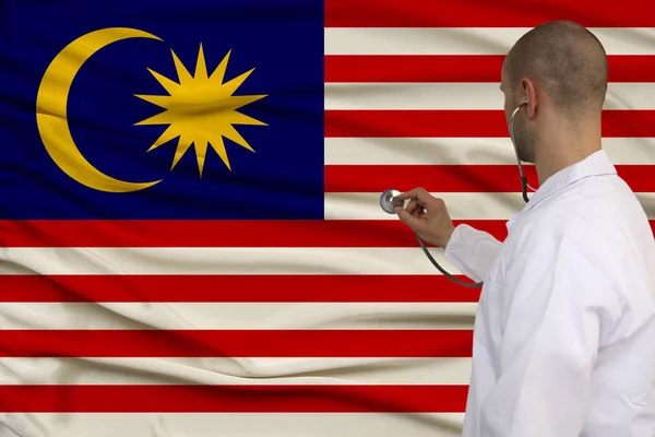 Partial photograph of the doctor in uniform against the background of the national malaysia flag on delicate shiny silk, the concept of medical care and insurance in the country, close-up, copy space — Stock Photo, Image