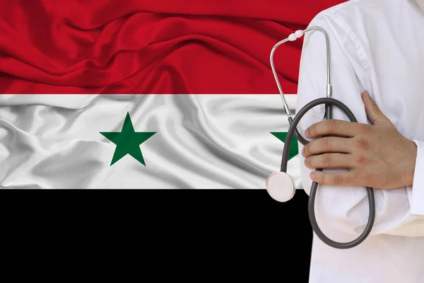 partial photograph of the doctor in uniform against the background of the Syria national flag on delicate shiny silk, the concept of medical care and insurance in the country, close-up, copy space