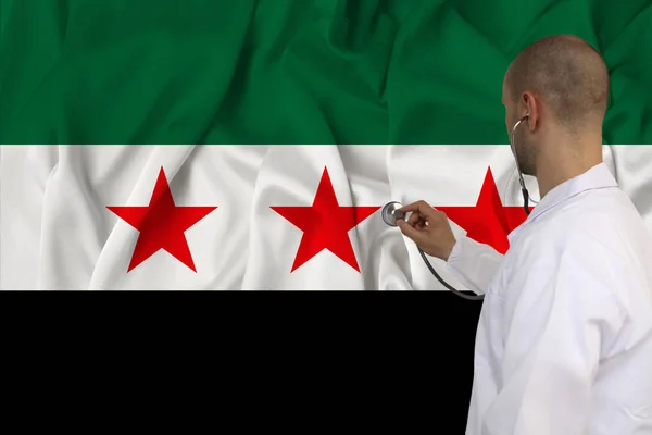 partial photograph of the doctor in uniform against the background of the Syrian opposition national flag on delicate shiny silk, the concept of medical care and insurance in the country, close-up, co
