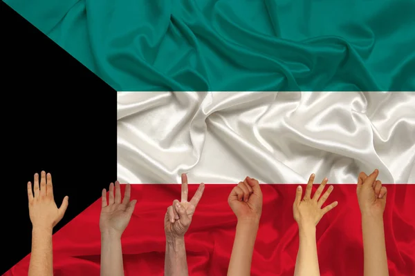 many hands raised up against the background of the Kuwait national flag on delicate shiny silk, concept of the country\'s population, unity, horizontal, close-up, copy space