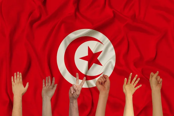 many hands raised up against the background of the national flag of Tunisia on delicate shiny silk, concept of the country\'s population, unity, horizontal, close-up, copy space