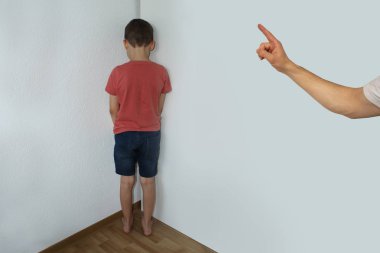 cezalı bir çocuk, bir ortaokul çocuğu, köşede duruyor, duvara bakıyor; bir ebeveynin eli suistimal için bir parmak yüzleri, eğitim kavramı