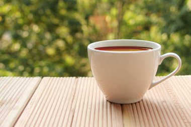 yeşil bir yaz bahçesi, yakın çekim, kopya alanı karşı açık ahşap bir masada kahve ile beyaz fincan