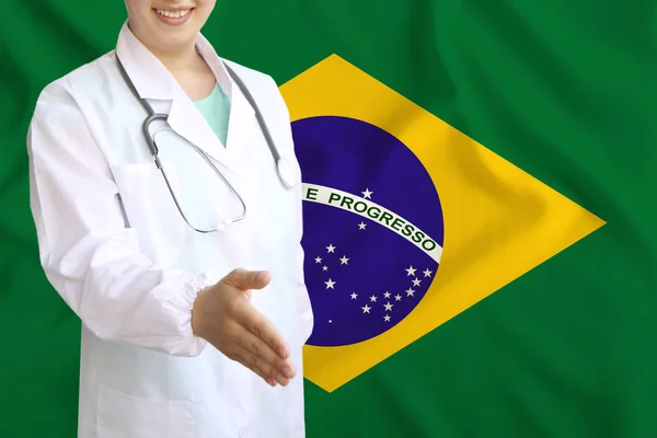 Joven hermosa niña médico con una sonrisa abierta extiende su mano para saludar en el fondo de la bandera nacional, conceptos de salud, medicina —  Fotos de Stock