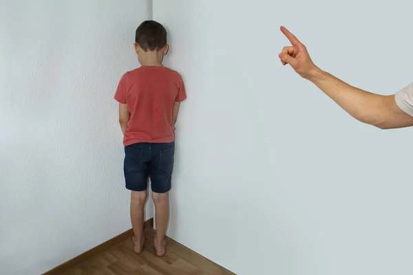 Um menino punido, um estudante júnior, está de pé no canto, de frente para a parede; a mão de um pai enfrenta um dedo por má conduta, o conceito de educação — Fotografia de Stock