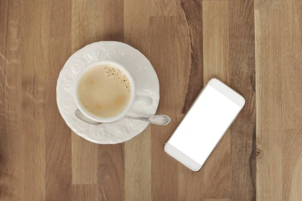 Mock up image of white mobile phone with empty white screen and a cup of coffee on a wooden table, top view