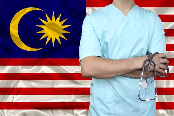 Fotografia parziale del medico in uniforme sullo sfondo della bandiera nazionale malaysia su seta lucida delicata, il concetto di assistenza medica e assicurazione nel paese, primo piano, spazio copia — Foto Stock