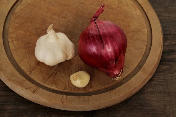 Zwiebeln, Knoblauch auf einem hölzernen runden Brett, Gemüsekonzept gegen Erkältungen, waagerecht, Nahaufnahme, Kopierraum — Stockfoto