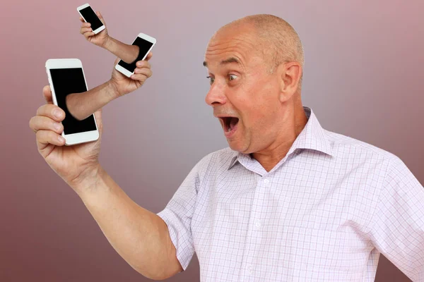 Homem tem um telefone na mão, a partir do qual uma mão se destaca com outro gadget, o conceito de tecnologia do absurdo, surrealismo, close-up, espaço de cópia — Fotografia de Stock
