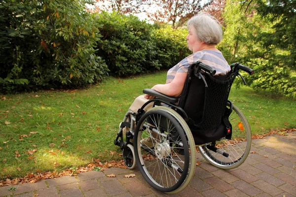 Одинокая парализованная женщина в инвалидной коляске сидит на улице и смотрит на природу — стоковое фото