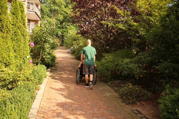 Joven lleva a una anciana con sobrepeso en una silla de ruedas en la calle —  Fotos de Stock