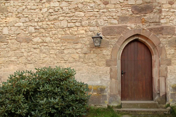 Áspero arenoso viejo muro de piedra medieval con puerta arqueada y linterna de hierro forjado. Fondo para el diseño, primer plano, espacio de copia . — Foto de Stock