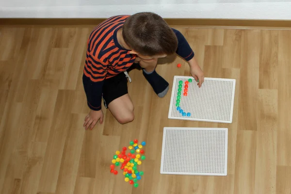 Boy, preschooler, collects patterns from colored mosaics, the development of fine motor skills of hands, sitting on the floor, top view, developing concept — Stock Photo, Image