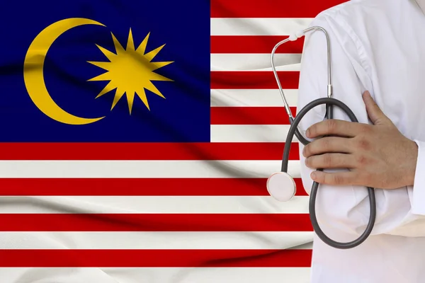 Partial photograph of the doctor in uniform against the background of the national malaysia flag on delicate shiny silk, the concept of medical care and insurance in the country, close-up, copy space — Stock Photo, Image