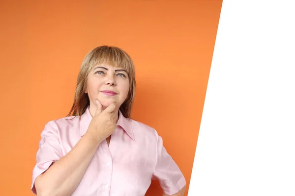 Mujer europea de mediana edad se para, sonríe, sobre un fondo naranja —  Fotos de Stock