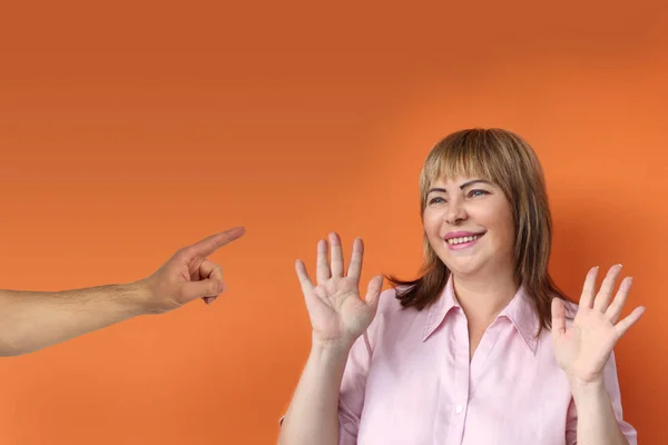 Европейская женщина средних лет стоит протестуя протягивая обе руки, мужская рука показывает обвинительный палец, оранжевый фон, крупный план, копировальное пространство — стоковое фото