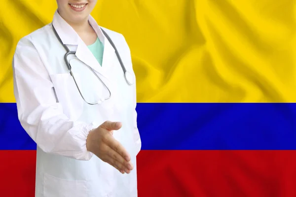 Joven hermosa niña médico con una sonrisa abierta extiende su mano para saludar en el fondo de la bandera nacional, conceptos de salud, medicina — Foto de Stock