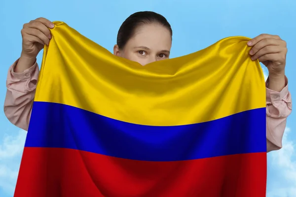 Niña sosteniendo en ambas manos una bandera nacional de color sobre hermosa seda brillante contra un cielo azul, concepto de estado, viajes, inmigración, horizontal, primer plano, espacio de copia — Foto de Stock