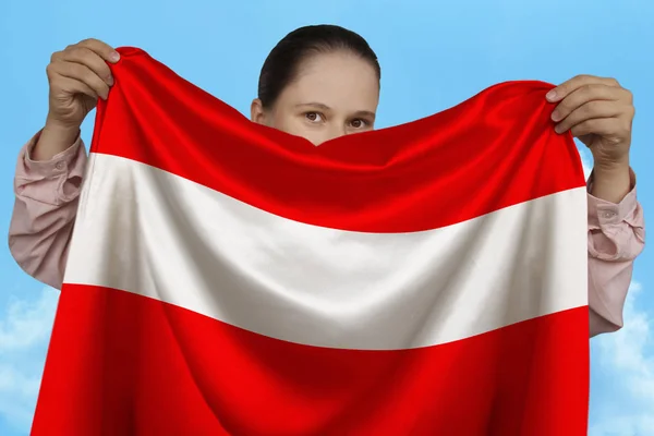 Gadis muda memegang di kedua tangan bendera nasional Austria pada sutra mengkilap indah melawan langit biru, konsep negara, perjalanan, imigrasi, horisontal, close-up, ruang fotokopi — Stok Foto