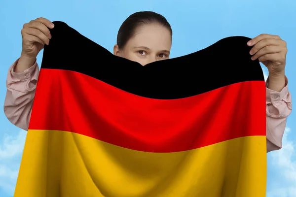 Молода дівчина тримає в обох руках Національний прапор Німеччини на красиві блискучі шовкові проти синього неба, державної концепції, подорожей, імміграції, горизонтальні, Крупний план — стокове фото