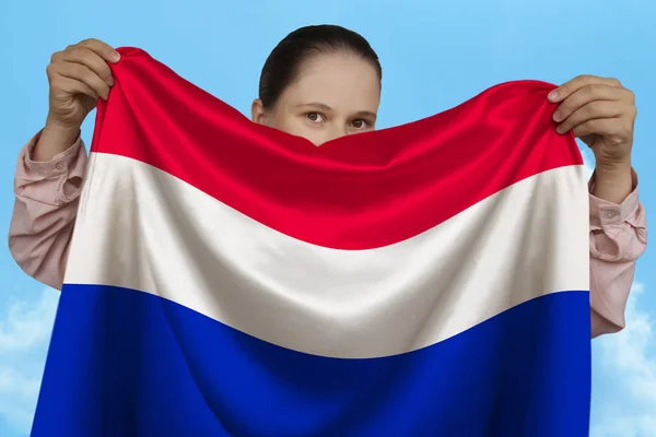 Gadis muda memegang di kedua tangan berwarna bendera nasional pada indah berkilau sutra terhadap langit biru, konsep negara, perjalanan, imigrasi, horisontal, close-up, salinan ruang — Stok Foto