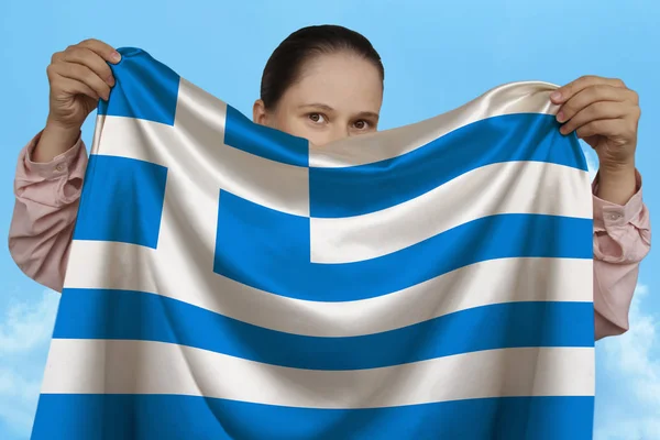 Young girl holding in both hands a colored national flag on beautiful shiny silk against a blue sky, state concept, travel, immigration, horizontal, close-up, copy space — Stock Photo, Image