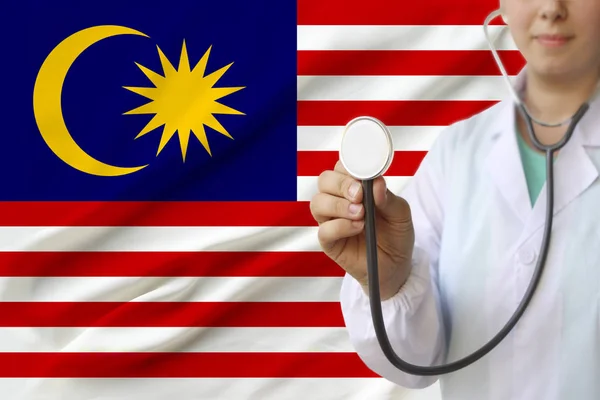 Partial photo of a girl doctor, nurse with a stethoscope in uniform against the background of the national flag of the state of Malaysia, the concept of medical care and insurance in the country — Stock Photo, Image