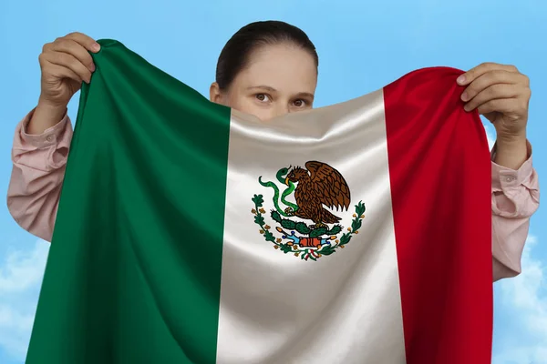 Fiatal lány gazdaságban mindkét kezében a nemzeti zászló Mexikó gyönyörű csillogó selyem ellen kék ég, az állami koncepció, utazás, a bevándorlás, vízszintes, közeli, másolási tér — Stock Fotó