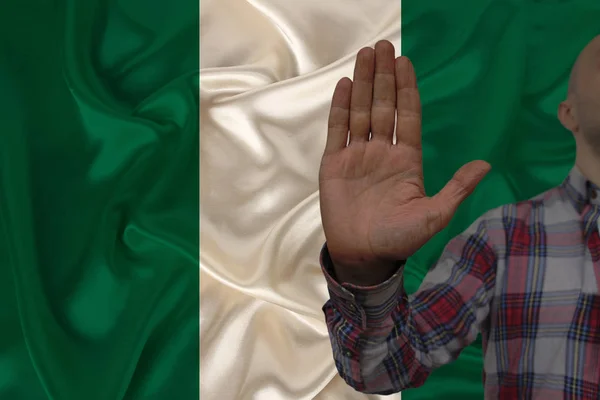 Mano masculina con un gesto de protesta, votos contra el fondo de la bandera nacional de seda de Nigeria, concepto de negación y prohibición y prohibición, primer plano, espacio para copiar — Foto de Stock