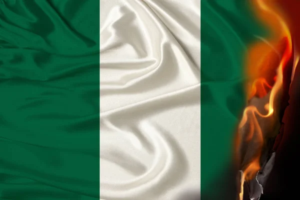 Llamas naranjas y cenizas sobre la orgullosa bandera nacional del estado de Nigeria, el concepto de revolución, guerra, golpe, destrucción, incendios en el país, primer plano — Foto de Stock