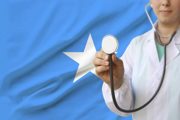 Fotografía parcial de una doctora, enfermera con un estetoscopio en uniforme en el fondo de la bandera nacional del estado de Somalia, el concepto de atención médica y seguro en el país — Foto de Stock