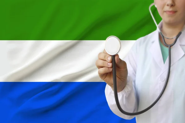 Fotografía parcial de un médico con un estetoscopio en uniforme profesional sobre el fondo de la bandera nacional del estado de Sierra Leona — Foto de Stock