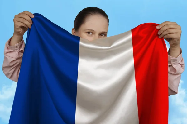 Young girl holding in both hands the national flag on beautiful shiny silk against a blue sky, state concept, travel, immigration, horizontal, close-up, copy space — Stock Photo, Image