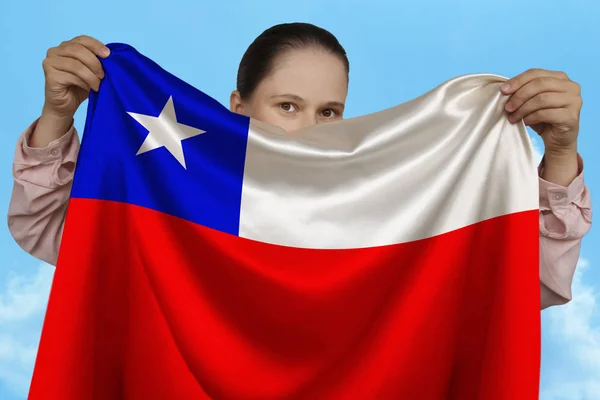 Fiatal lány gazdaságban mindkét kezében a nemzeti zászló gyönyörű csillogó selyem ellen kék ég, az állami koncepció, utazás, a bevándorlás, vízszintes, közeli, másolási tér — Stock Fotó