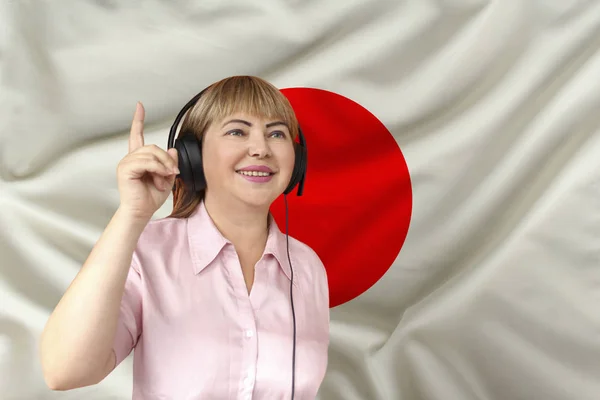 Žena ve sluchátkách proti pozadí národní vlajky Japonska na jemnému lesklém hedvábí, koncept volného vzduchu, hudby, zpravodajství, podcastu, horizontální, těsné, kopírovací místo — Stock fotografie