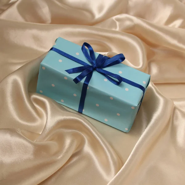 Gift in colored paper, tied with satin ribbons on a luxurious texture of satin, silk with waves, folds and highlights, congratulatory, holiday concept, horizontal, close-up, copy space — Stock Photo, Image