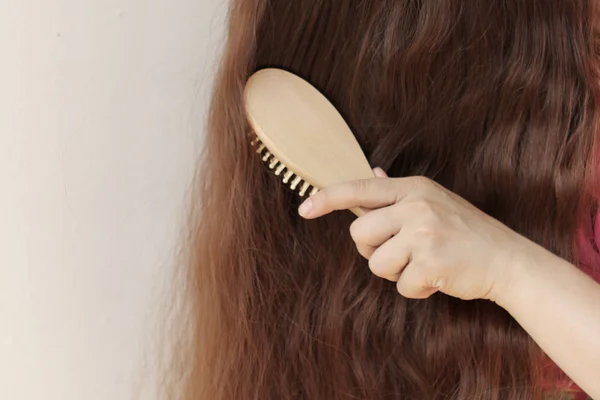 Chica con el pelo largo peinándolos con un peine de madera, horizontal, primer plano — Foto de Stock