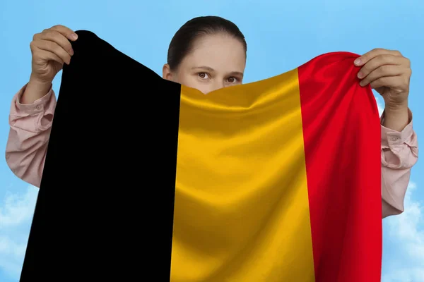 Junges Mädchen, das in beiden Händen die belgische Nationalflagge auf wunderschöner, glänzender Seide vor blauem Himmel hält, Staatskonzept, Reisen, Einwanderung, Horizontal, Nahaufnahme, Kopierraum — Stockfoto