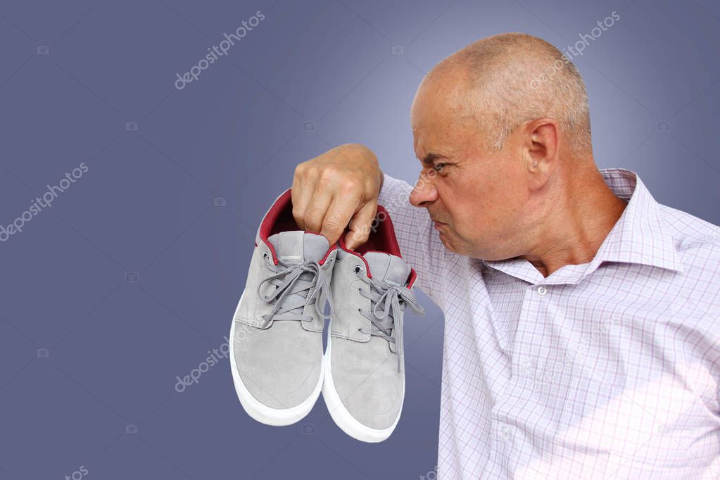 man in a light shirt holds a pair of gray male moccasins in his hand and sniffs it, a grimace of disgust from the bad smell on his face, close-up, copy space