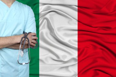 Steteskoplu profesyonel üniformalı erkek doktor, ulusal bayrağın arka planına, ülkenin sağlık ve sağlık sigortası kavramına, yakın plan, fotokopi alanına karşı duruyor.