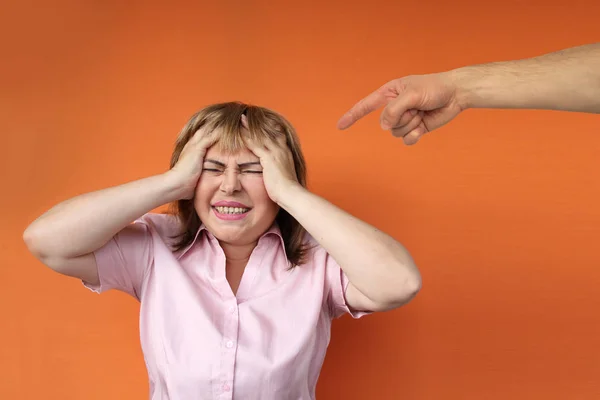 Mulher europeia de meia-idade está protestantemente estendendo ambas as mãos, mão masculina mostra dedo acusatório, fundo laranja, close-up, espaço de cópia — Fotografia de Stock