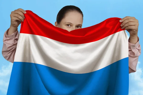 Jong meisje holding in beide handen een gekleurde nationale vlag op mooie glanzende zijde tegen een blauwe hemel, staat concept, reizen, immigratie, horizontaal, close-up, kopieer ruimte — Stockfoto