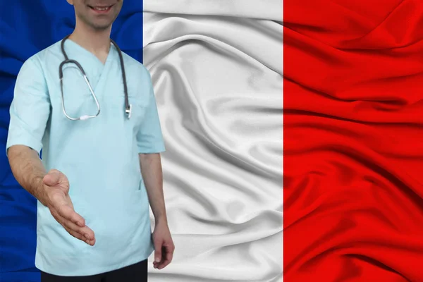 Mužský lékař v uniformních profesionálních šatech s stetoskem vítá pacienty s rukou na pozadí národní vlajky, pojetí zdravotního a lékařského pojištění země — Stock fotografie