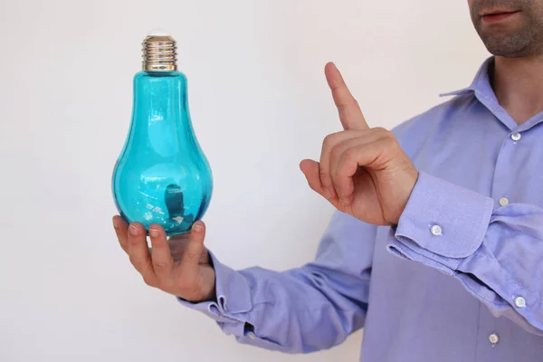 Forretningsmann i blå skjorte har en stor blå glasslampe i hånden, fingeradvarsel, elektrisitetskonsept, ideer, kopieringsrom – stockfoto