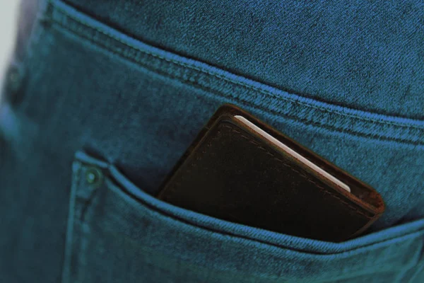 Donker bruine heren portemonnee gemaakt van hoogwaardig echt leer ligt in de achterzak van grijze jeans voor mannen, afgezwakt in een turquoise kleurenfoto — Stockfoto