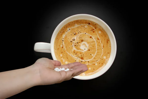 Mão feminina derrama pílulas brancas em uma ampla xícara branca de café, um cappuccino em forma de avião em um fundo preto com vinheta, vista superior, economizar espaço, close-up, veneno conceito, envenenamento — Fotografia de Stock