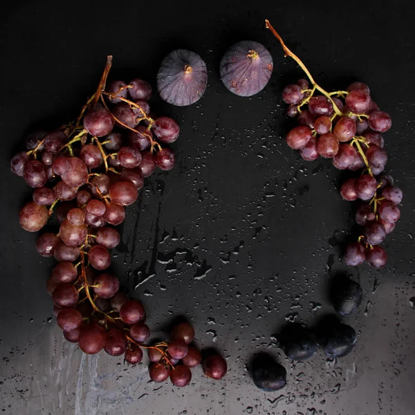 黒いブドウと紫のイチジクの美しいクラスターは、滴、水の飛沫、クローズアップ、ビタミンコンセプト、ビーガン食品、健康的な食事、コピースペースと黒いテーブルの上に — ストック写真