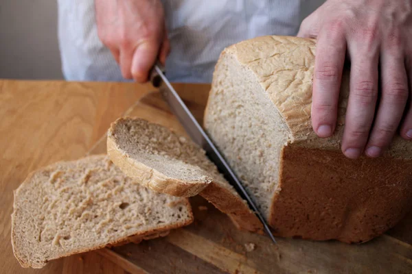 Man houdt een groot keukenmes in zijn hand en snijdt ermee vers gebakken, geurig, knapperig roggebrood, een symbool van voedsel, kopieer ruimte — Stockfoto