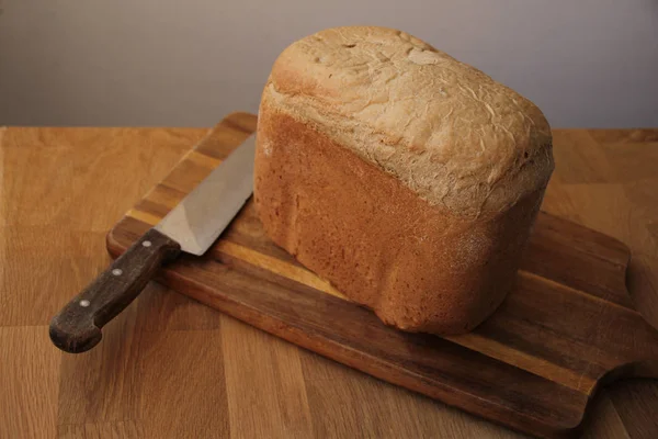 Grande faca de cozinha e pão caseiro em uma placa de corte entorpecida esfria, close-up, espaço de cópia — Fotografia de Stock